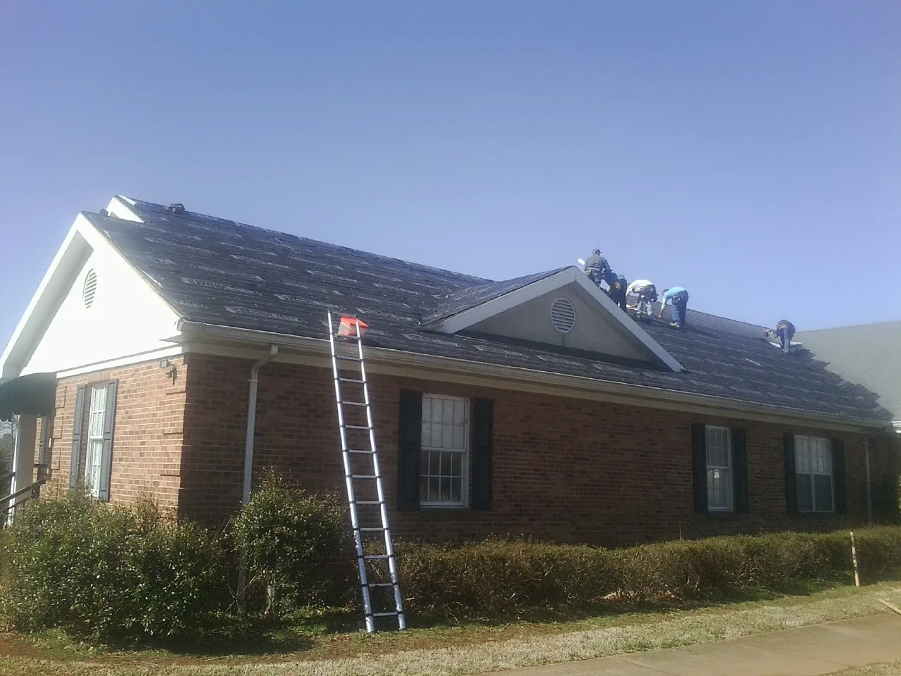 Crew tearing shingles off a brick ranch roof with a ladder set — Emergency Roof Repair work by our crew in Forest Falls