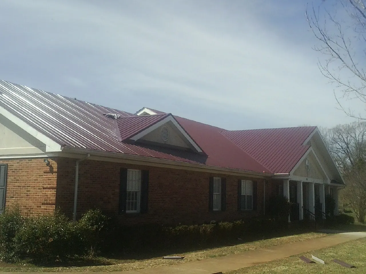 Red metal roof with gabled entries on a long brick building, from a Hail Damage Roof Repair job in Forest Falls