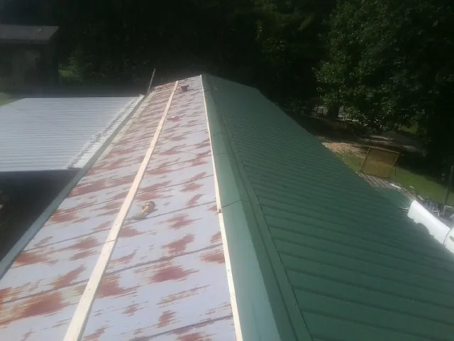 Old rusted panels beside newly installed green metal roofing — Wind Damage Roof Repair by Roofing Brothers in Forest Falls