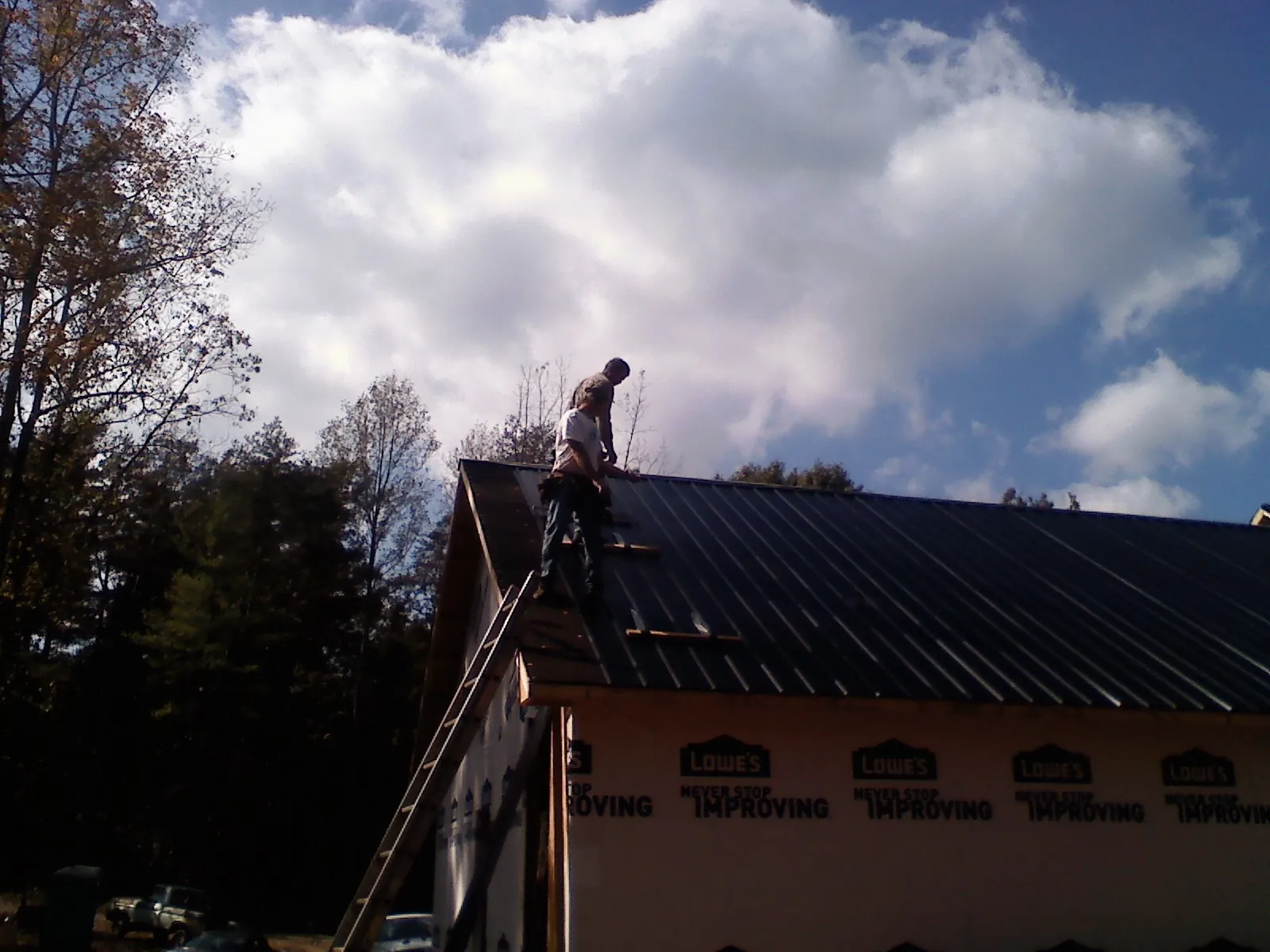 Roofer fastening dark metal panels high against a cloudy sky, from a Roof Inspection job in Forest Falls