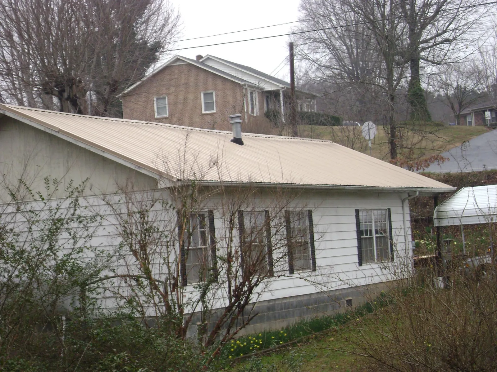 Tan metal roof on a white sided house set into a hillside — Commercial Roofing by Roofing Brothers in Forest Falls
